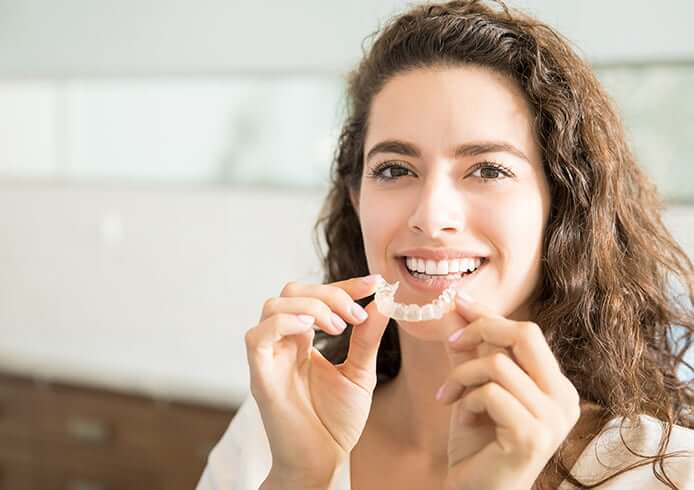 woman insterting a set of clear aligners onto her teeth