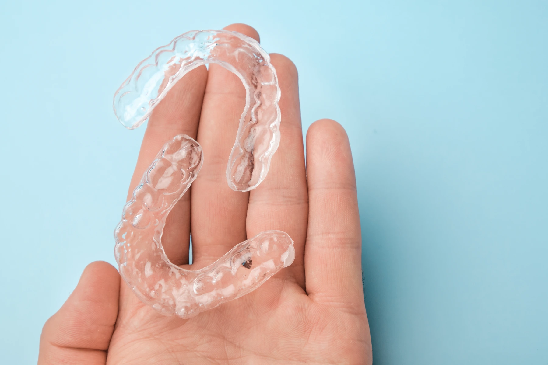 hand holding a pair of invisalign with a light blue background